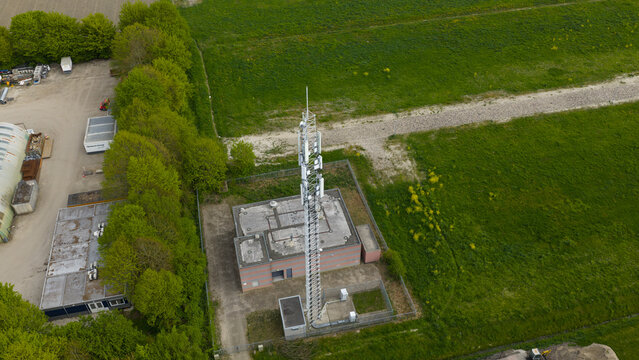 Aerial view of a telecommunications tower and utility building surrounded by lush green fields and a row of trees near Watersnipweg in Almere, Flevoland, Netherlands.