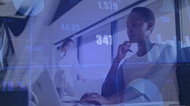 Woman typing and pausing, pen at chin, laptop in tech office animating blue charts, reviewing data