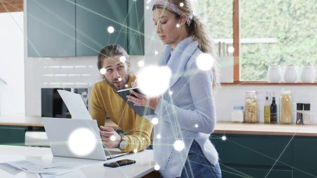 Couple reviewing finance in kitchen using devices, sparking nodes blooming over them then fading