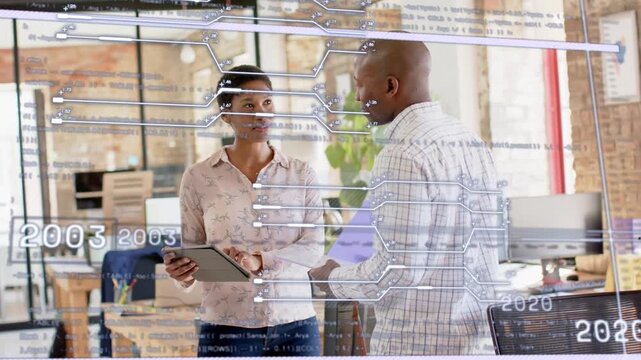 Woman pointing tablet starting timeline on glass while man tracing glass, reviewing 2013 tech plan