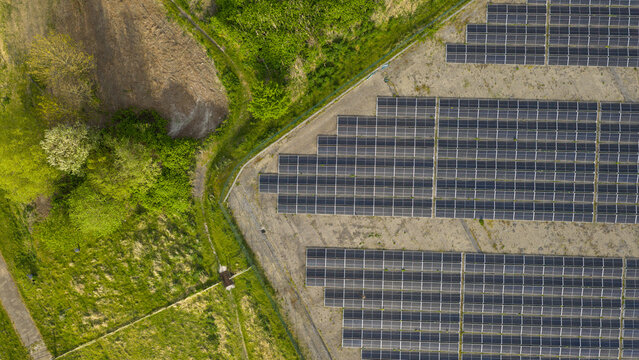 Aerial view of the Zonnepark Braambergen solar farm with rows of photovoltaic panels next to green fields and trees in Almere, Flevoland, Netherlands.