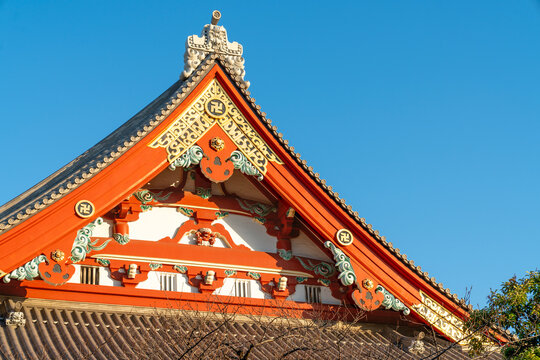 Ornate red and gold roof detail of a traditional Japanese Buddhist temple in Tokyo against a clear blue sky. Intricate architectural craftsmanship and cultural heritage of Japan's historic shrines.