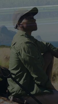 Vertical video: Man sitting dune by sea, bag+pole left, light streaks causing gaze up for travel