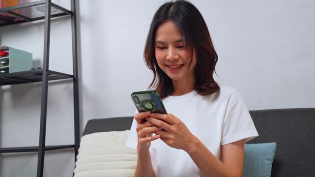 Asian woman using mobile phone for browsing and texting at home in a relaxed lifestyle moment.