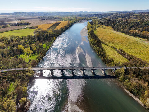 Aerial view of the Po River flowing through the Parco Fluviale del Po with a stone bridge, surrounded by autumn-colored fields and forests Trino, Piedmont, Italy.