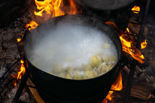 Dumplings boil intensely in pot over direct flame, producing thick foam aromatic steam that gathers people around outdoor fire pit