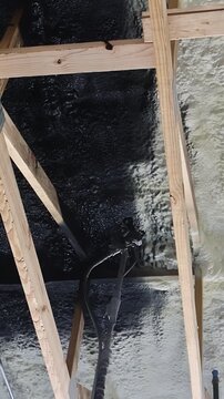Contractor in protective gear applies refractory paint insulation using spray gun to wooden ceiling beams at construction site.