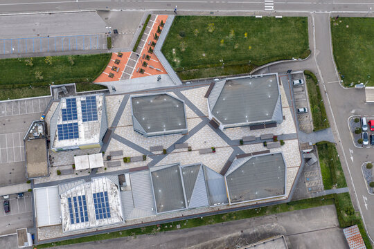Aerial view of a modern commercial building complex featuring geometric rooftops with solar panels and a paved courtyard in Reggello, Tuscany, Italy.
