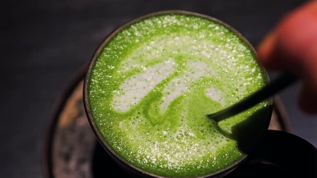 Adding brown sugar cube to a warm cup of matcha latte, stirring to dissolve, close up motion footage.