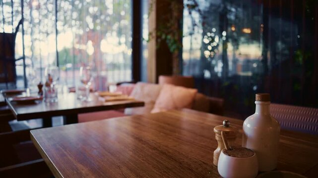 Empty cozy restaurant interior with wooden tables set for dinner, bokeh lights outdoor, dynamic motion.
