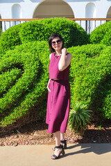 young woman summer dress stands near neatly trimmed green bushes. © ALEXEY