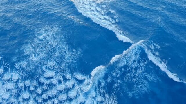 Waves crash on ocean surface creating white foam in deep blue water