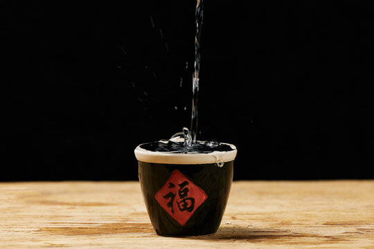 Pouring clear liquor into traditional Chinese wine jar on wooden table