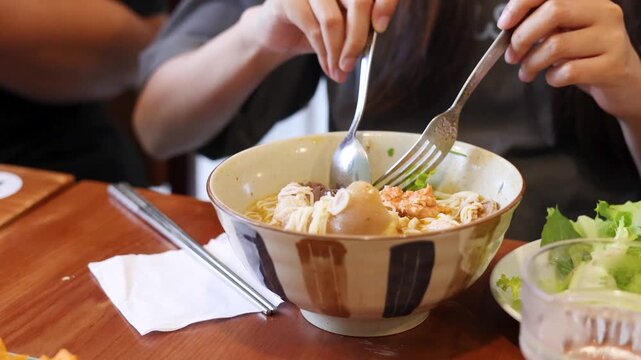 A close up shot of a young person enjoying a delicious bowl of vietnamese pho noodles with pork hock, pork blood, and various toppings at a restaurant.