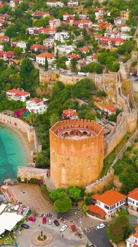 Vertical video. Alanya, Turkey. Kizilkule Red Tower as part of medieval defense system with Alanya Tersanesi shipyard and fortress walls.. Aerial View, Departure of the camera, MasterShots. Rich colo