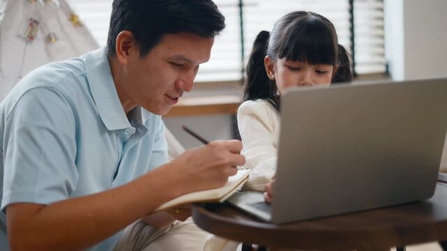Asian father teaching daughter doing homework,online learning on laptop computer at home.Parents homeschooling and supporting girl during summer break.Concept of online education and online learning
