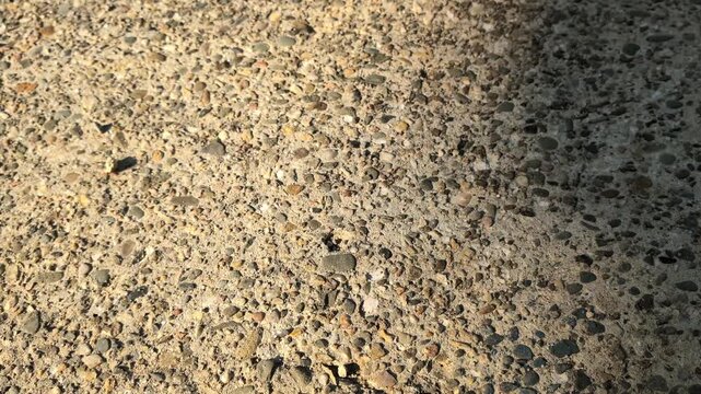 Horizontal cinematic pan of weathered cracked concrete pavement with exposed aggregate. Industrial background of aged building surface with structural damage and rough grey plaster textures.