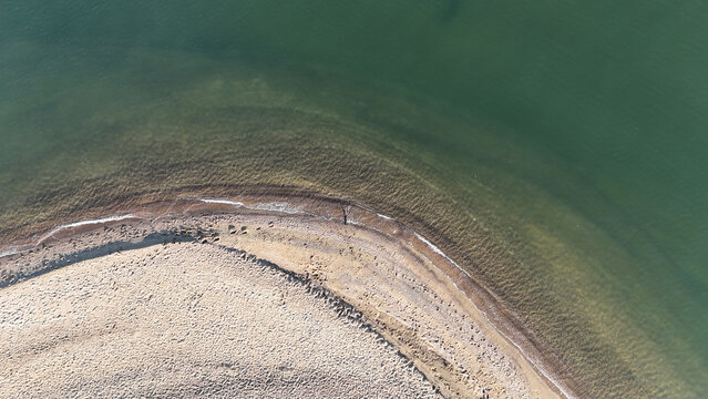 Aerial view of the curved sandy shoreline of Sandy Point State Park meeting the calm green waters of the Chesapeake Bay in Annapolis, Maryland, United States.