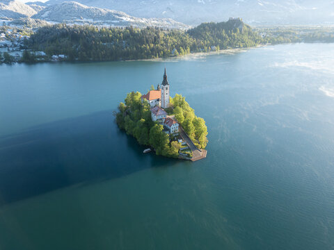 Aerial view of Lake Bled island and the Pilgrimage Church of the Assumption of Mary with Bled Castle and snowy mountains in the background at Bled, Radovljica, Slovenia.
