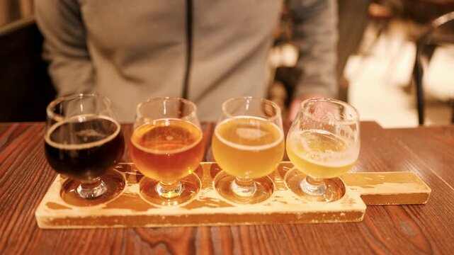 Person sampling flight of craft beers on wooden paddle at tasting table.