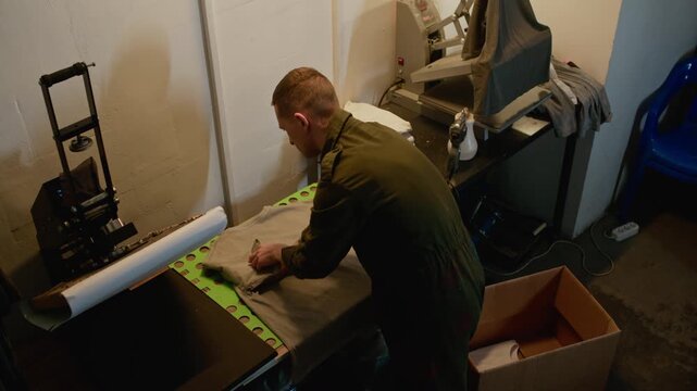Overhead view of man neatly folding grey t shirts on worktable in printing workshop, showing final stage of apparel production and packaging process
