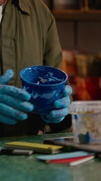 Vertical tilt down shot of male designer picking blue paint jar and using spatula to prepare screen printing materials