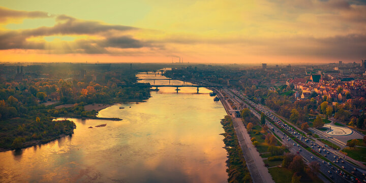 Aerial view of the Vistula River flowing through the city with historic bridges and autumn trees during a golden sunset Warsaw, Masovian Voivodeship, Poland.