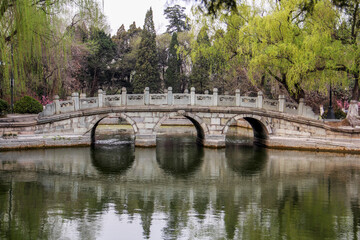 Fototapeta premium Stone arch bridge over calm water with surrounding trees