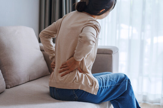 Woman suffering from back pain while sitting on the couch at home, Health care and medical concept