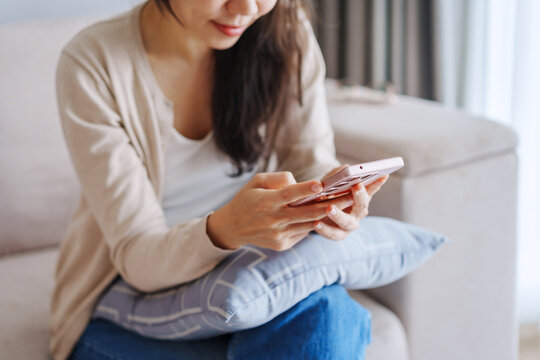 Young Asian woman relaxing and using mobile phone on a sofa at home in the morning