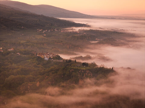 Aerial view of the historic village of Piantravigne perched on a hill surrounded by thick morning mist and rolling hills at sunrise Piantravigne, Tuscany, Italy.
