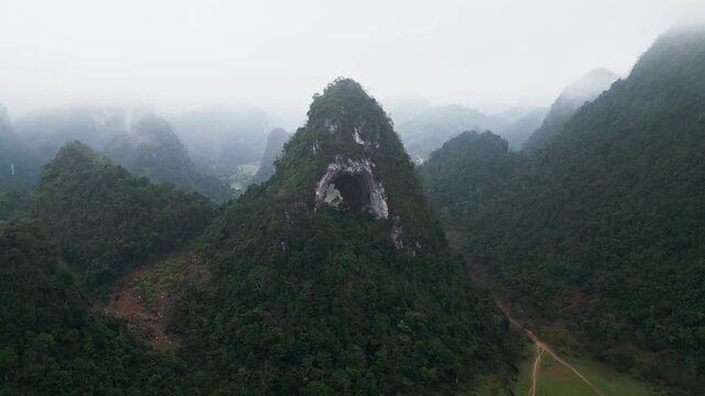 Aerial drone footage of misty karst hills in steady rain with thick fog drifting through forested peaks, forming a dark atmospheric landscape with strong moody tones.