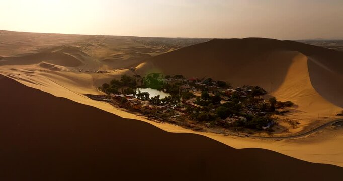 Huacachina natural desert oasis village among dunes in Peru at sunset, aerial