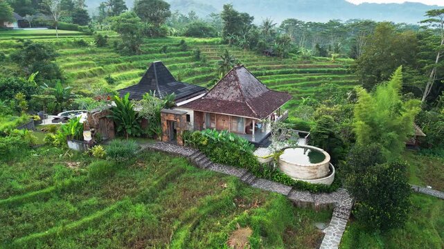 Aerial drone footage of a traditional Joglo villa set among lush rice terraces and tropical greenery with a private pool overlooking a scenic hillside landscape in Sidemen Bali