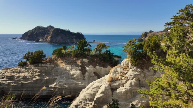 Scenic overlook of the striking white volcanic tuff cliffs and turquoise waters of Dogashima, featuring the Sanshiro Islands under a clear blue sky in Izu, Japan