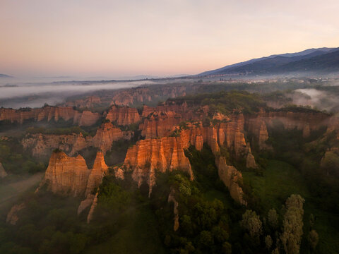 Aerial view of Le Balze del Valdarno rock formations shrouded in morning mist with golden sunrise light hitting the clay pinnacles and green forests Botriolo, Toscana, Italy.