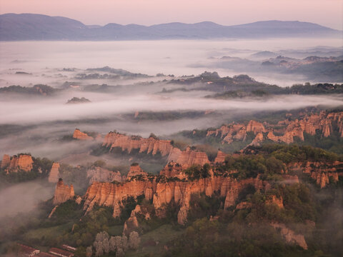 Aerial view of Le Balze del Valdarno rock formations emerging from thick morning fog with rolling hills in the background Botriolo, Toscana, Italy.