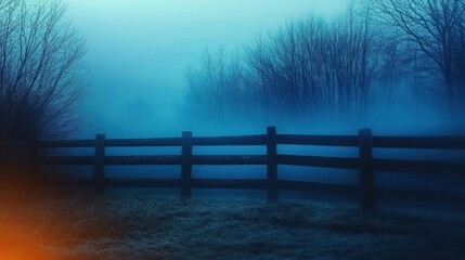 Obraz premium wooden fence across a frosty field with bare trees shrouded in blue fog and a distant warm orange glow, evoking quiet, mysterious solitude