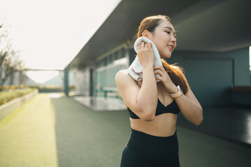 Fitness woman wiping sweat with a towel after outdoor workout, representing recovery, cooling down,...