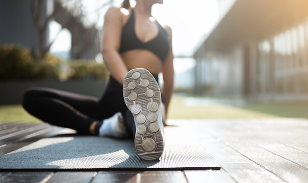 Woman stretching outdoors on a yoga mat during workout, representing flexibility, balance, and a healthy active lifestyle in natural sunlight.
