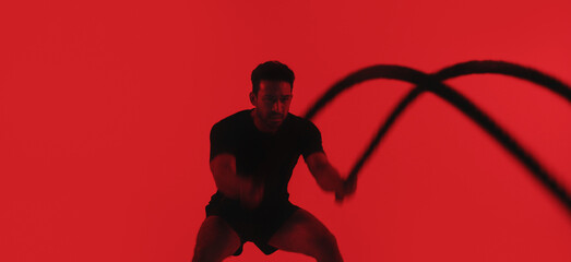 Man, fitness and battle rope in studio with exercise, strength training and intense physical activity. Mockup space, person and workout with endurance challenge, cardio or wellness on red background © peopleimages.com