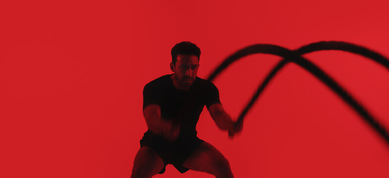 Man, fitness and battle rope in studio with exercise, strength training and intense physical activity. Mockup space, person and workout with endurance challenge, cardio or wellness on red background