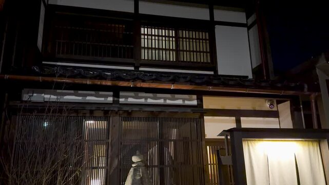 Traditional japanese machiya townhouse exterior at night with stone lantern and wooden lattice windows.