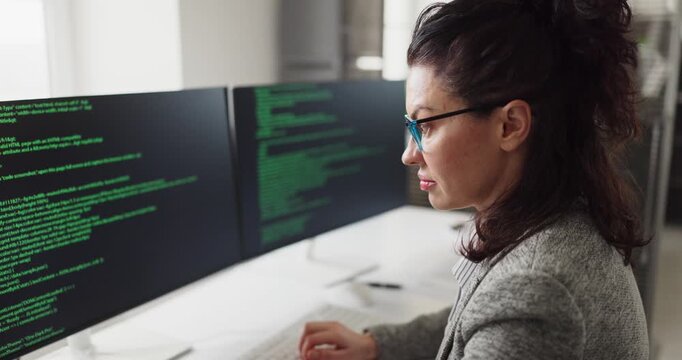 Businesswoman developer coding software on computer. She codes at dual monitors in an office, showing productivity, focus, and agile workflow for tech. Clear concept of modern coding work.