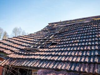 Naklejka premium Old damaged roof with broken concrete tiles and visible structural decay. Concept of house repair, maintenance, renovation, risk and property damage. 