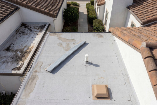 High angle view of a flat roof section showing water stains, a metal flashing piece, and a vent