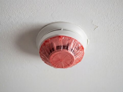 Smoke detector covered with a red plastic dust cover on a white ceiling
