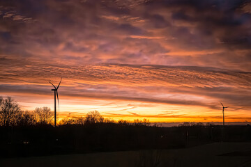 Obraz premium Die Nacht zieht sich langsam zurück wie ein schwerer Vorhang, und dahinter glüht der Himmel in flüssigem Gold und flammendem Kupfer. Die Windräder stehen wie stille Wächter am Horizont, ihre Flügel sc