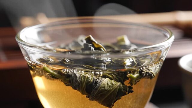 Closeup of blooming tea leaves unfurling in hot water inside a clear glass cup.