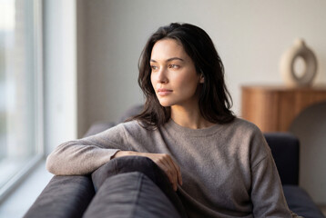 Obraz premium Calm woman relaxing on sofa looking out window in bright modern living room